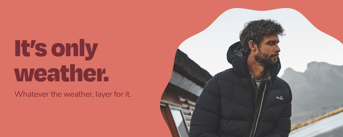 A man wearing a black puffer jacket stands outdoors with mountains in the background, set against a coral-red graphic layout with the text 'It's only weather. Whatever the weather, layer for it.