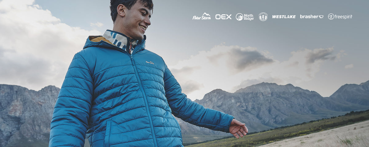 A man wearing a bright blue puffer jacket stands outdoors in front of mountains under a cloudy sky, with brand logos for DEX, Westlake, Brashler, and Freepalt displayed across the top right.